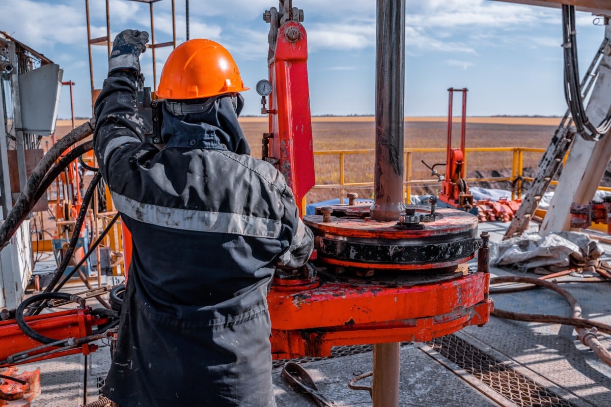 A roughneck in an orange hard hat working with red drilling equipment on the rig floor
